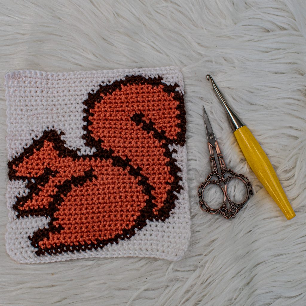 Tapestry crochet square of a squirrel, hook and scissors